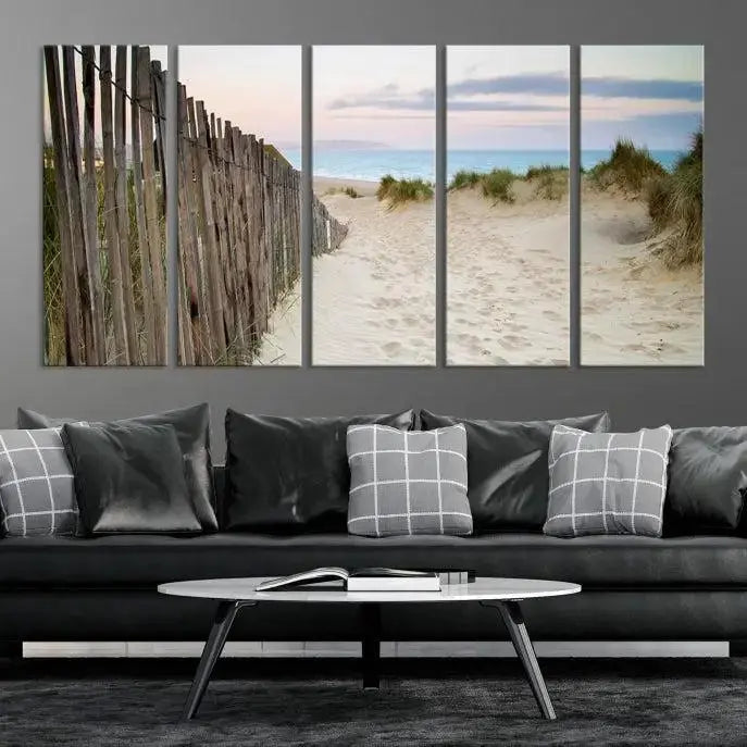 The Coastal Beach Fence Wall Art Ocean Landscape Canvas Print, featuring a triptych of a sandy beach scene with dunes and fences, is gallery wrapped on museum-quality canvas and displayed on a modern dark wall.