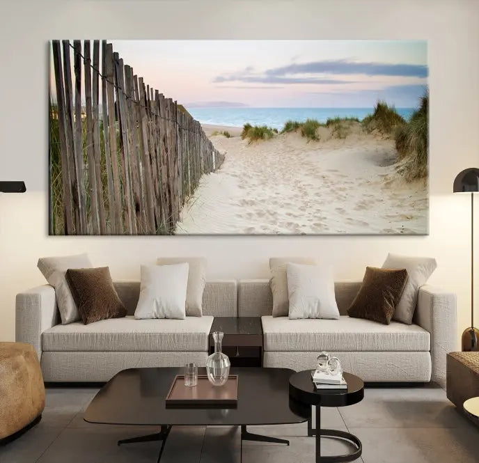 The Coastal Beach Fence Wall Art Ocean Landscape Canvas Print, featuring a triptych of a sandy beach scene with dunes and fences, is gallery wrapped on museum-quality canvas and displayed on a modern dark wall.