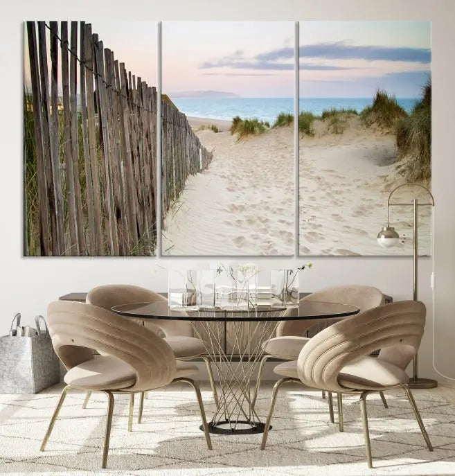 The Coastal Beach Fence Wall Art Ocean Landscape Canvas Print, featuring a triptych of a sandy beach scene with dunes and fences, is gallery wrapped on museum-quality canvas and displayed on a modern dark wall.