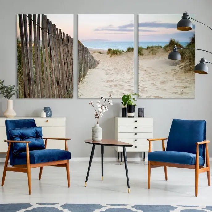 The Coastal Beach Fence Wall Art Ocean Landscape Canvas Print, featuring a triptych of a sandy beach scene with dunes and fences, is gallery wrapped on museum-quality canvas and displayed on a modern dark wall.