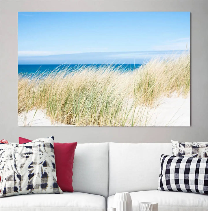 The Coastal Ocean Beach Wall Art Canvas Print, featuring a three-panel design with beach grass and an ocean view on museum-quality canvas, enhances the space in a modern living room. The artwork is ready to hang and comes with a UV-protective coating for enduring beauty.