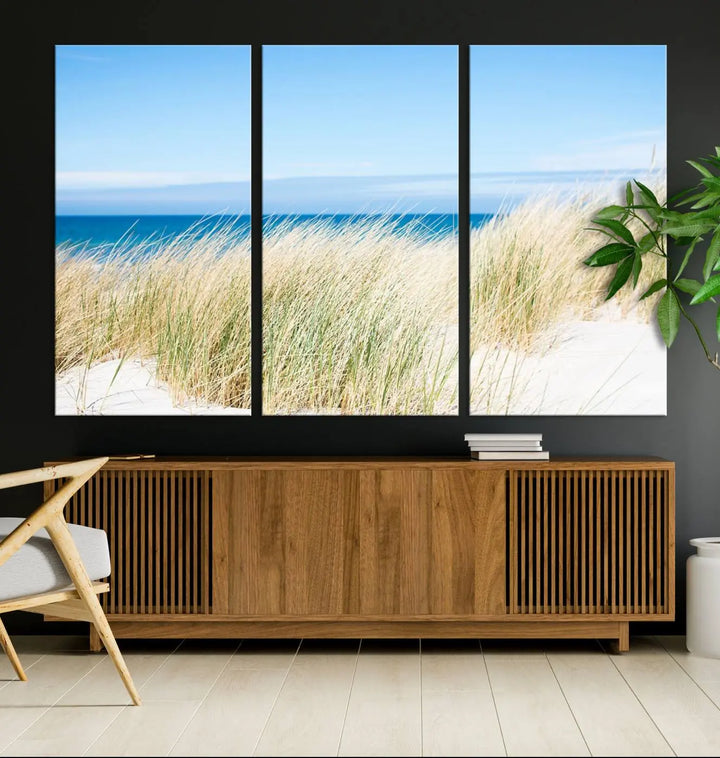 The Coastal Ocean Beach Wall Art Canvas Print, featuring a three-panel design with beach grass and an ocean view on museum-quality canvas, enhances the space in a modern living room. The artwork is ready to hang and comes with a UV-protective coating for enduring beauty.