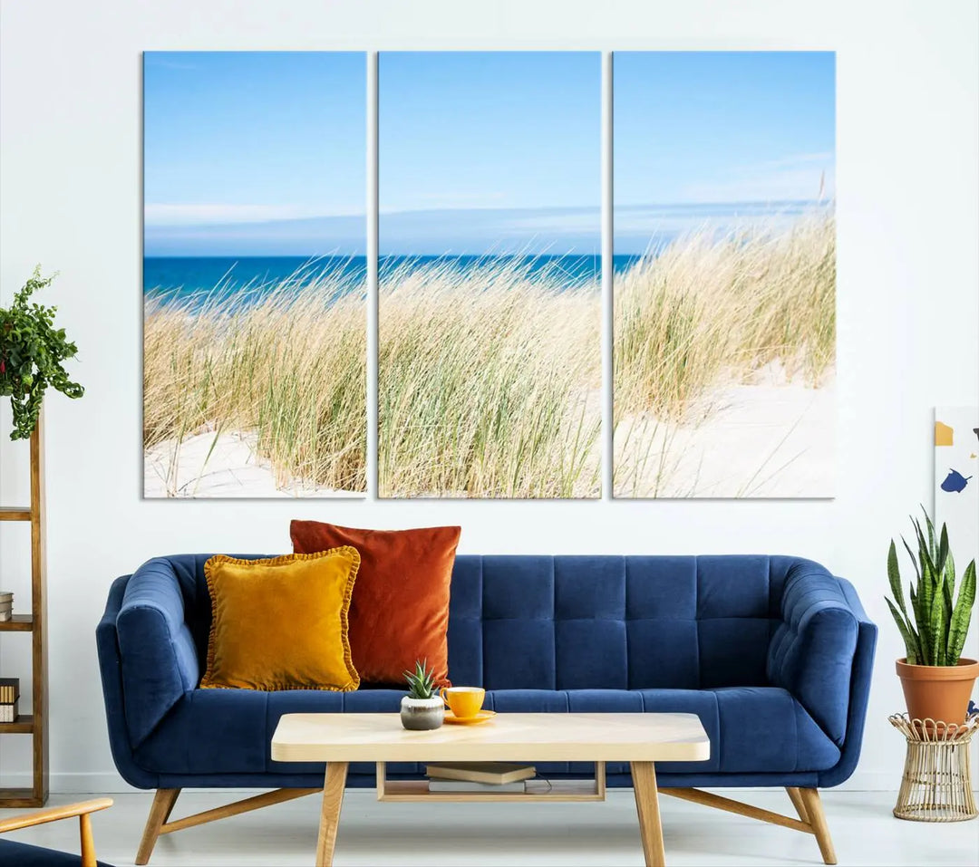 The Coastal Ocean Beach Wall Art Canvas Print, featuring a three-panel design with beach grass and an ocean view on museum-quality canvas, enhances the space in a modern living room. The artwork is ready to hang and comes with a UV-protective coating for enduring beauty.