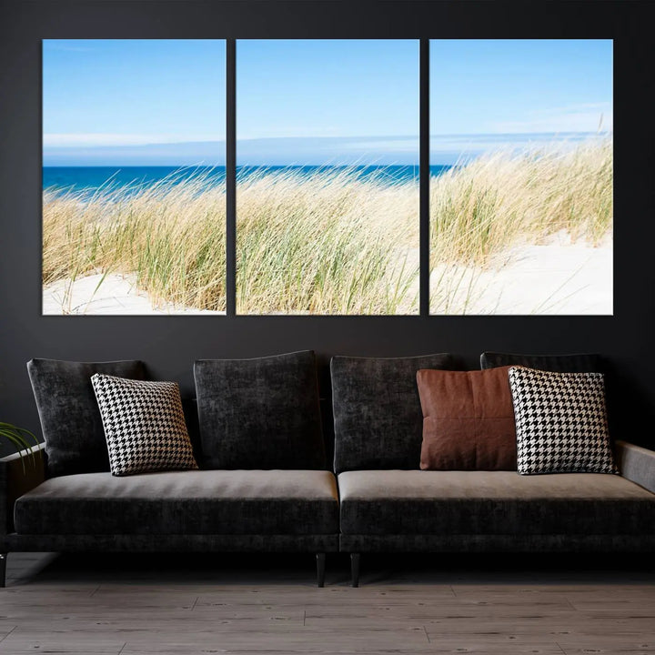 The Coastal Ocean Beach Wall Art Canvas Print, featuring a three-panel design with beach grass and an ocean view on museum-quality canvas, enhances the space in a modern living room. The artwork is ready to hang and comes with a UV-protective coating for enduring beauty.