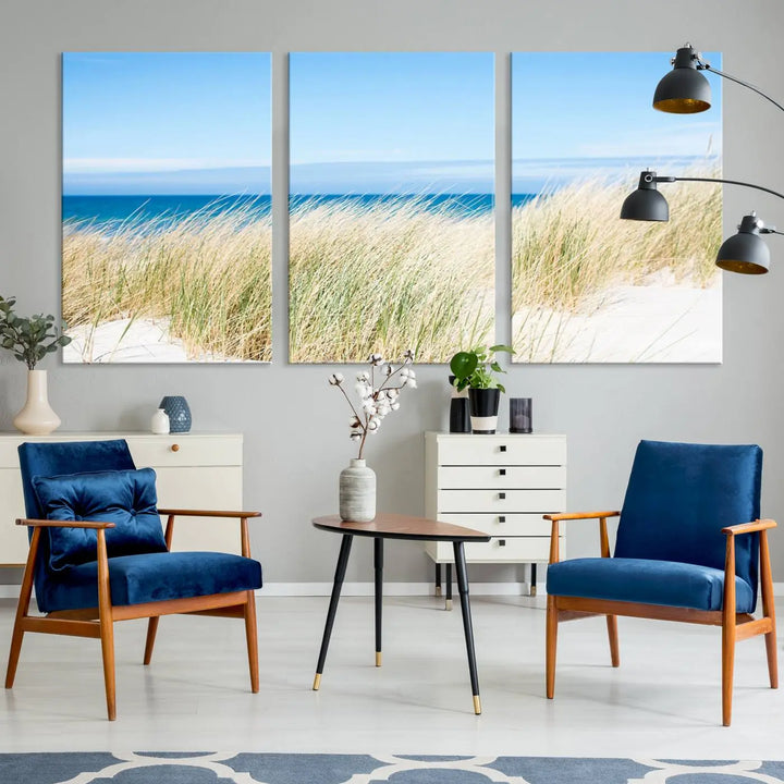 The Coastal Ocean Beach Wall Art Canvas Print, featuring a three-panel design with beach grass and an ocean view on museum-quality canvas, enhances the space in a modern living room. The artwork is ready to hang and comes with a UV-protective coating for enduring beauty.