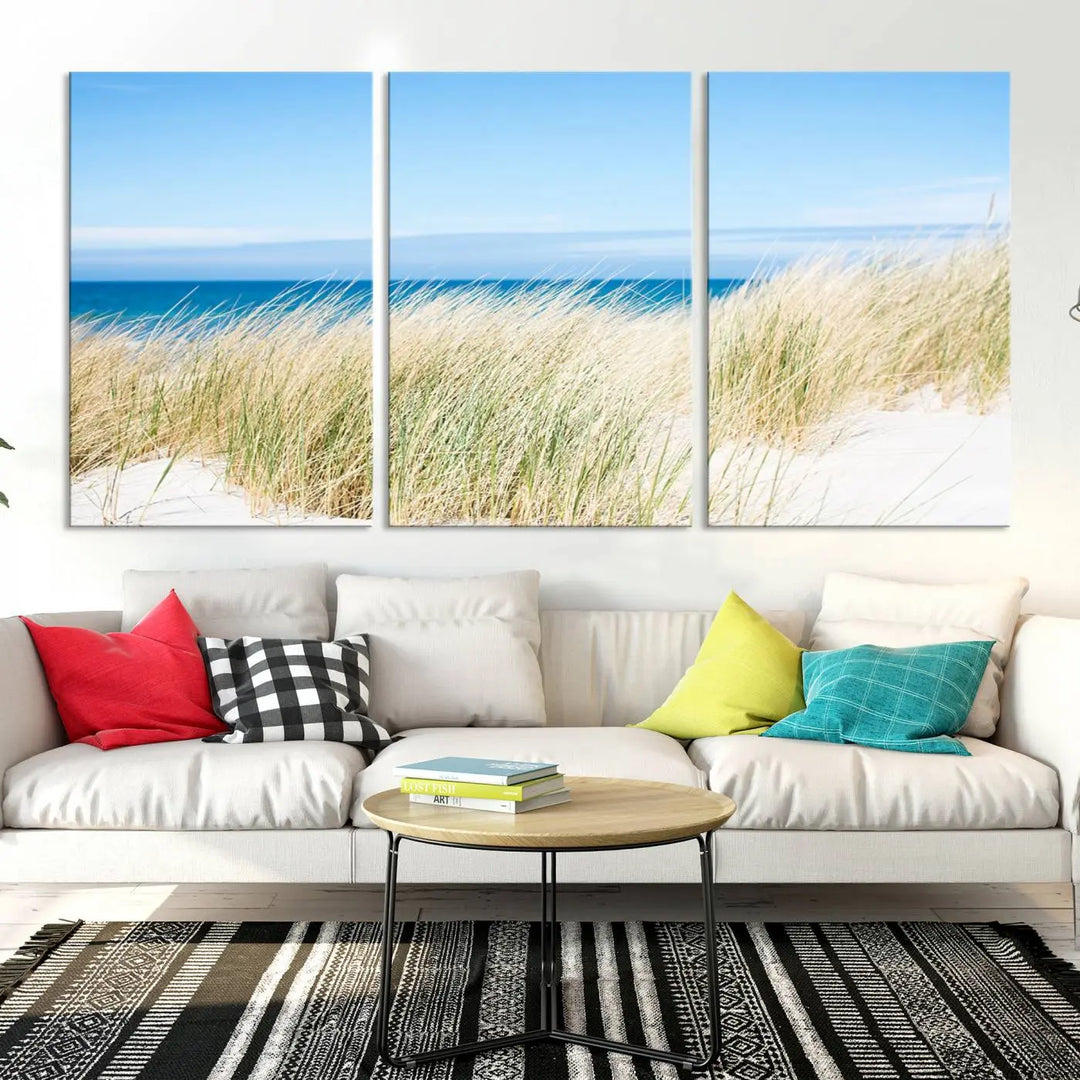 The Coastal Ocean Beach Wall Art Canvas Print, featuring a three-panel design with beach grass and an ocean view on museum-quality canvas, enhances the space in a modern living room. The artwork is ready to hang and comes with a UV-protective coating for enduring beauty.