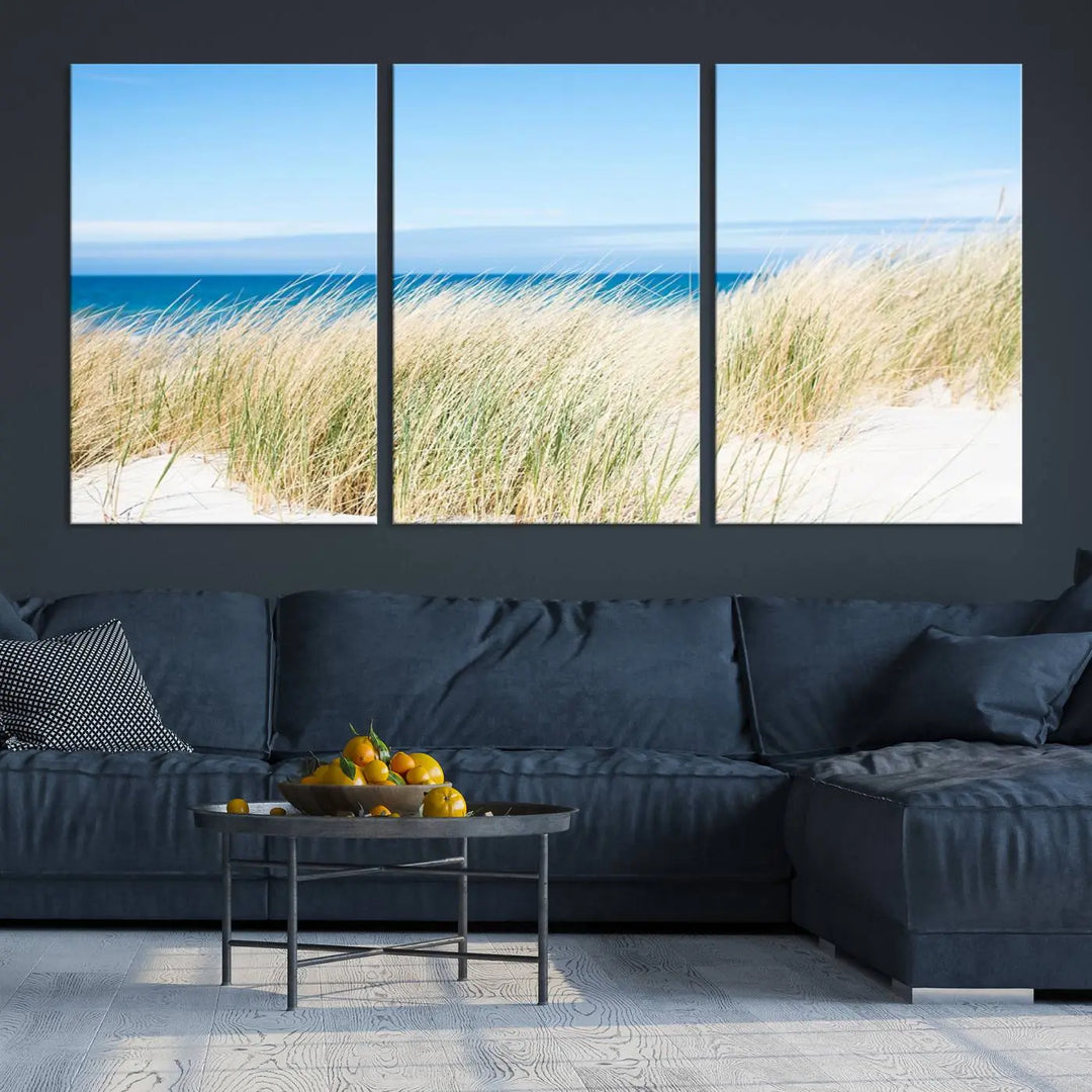 The Coastal Ocean Beach Wall Art Canvas Print, featuring a three-panel design with beach grass and an ocean view on museum-quality canvas, enhances the space in a modern living room. The artwork is ready to hang and comes with a UV-protective coating for enduring beauty.