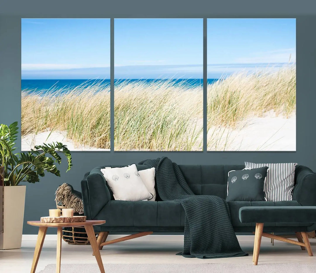 The Coastal Ocean Beach Wall Art Canvas Print, featuring a three-panel design with beach grass and an ocean view on museum-quality canvas, enhances the space in a modern living room. The artwork is ready to hang and comes with a UV-protective coating for enduring beauty.