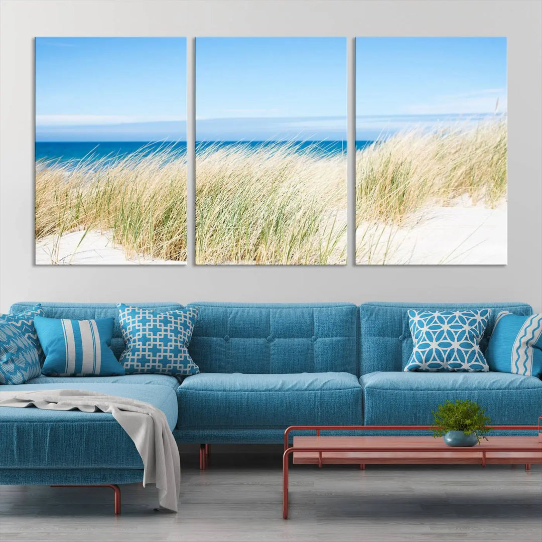 The Coastal Ocean Beach Wall Art Canvas Print, featuring a three-panel design with beach grass and an ocean view on museum-quality canvas, enhances the space in a modern living room. The artwork is ready to hang and comes with a UV-protective coating for enduring beauty.