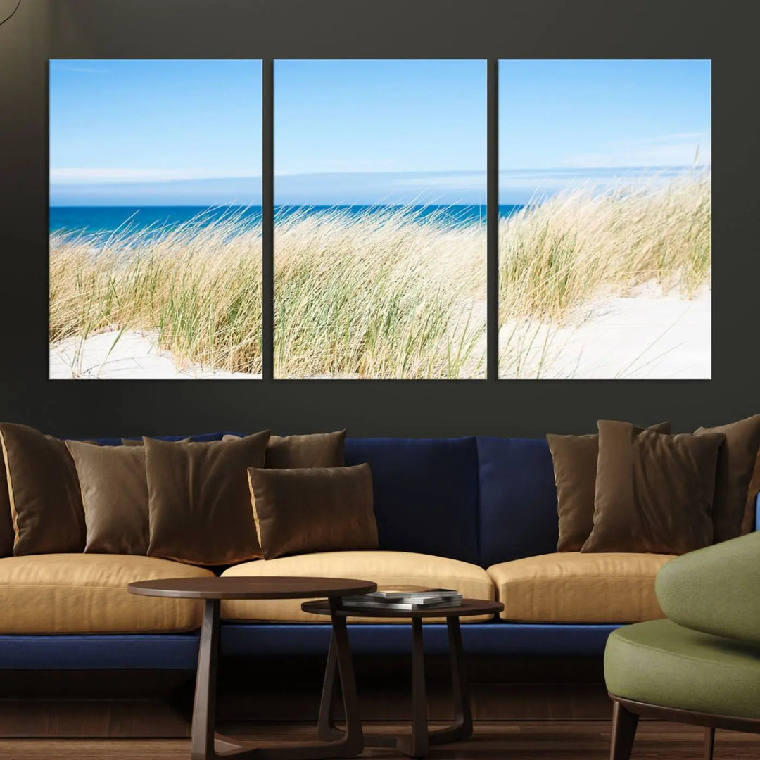 The Coastal Ocean Beach Wall Art Canvas Print, featuring a three-panel design with beach grass and an ocean view on museum-quality canvas, enhances the space in a modern living room. The artwork is ready to hang and comes with a UV-protective coating for enduring beauty.