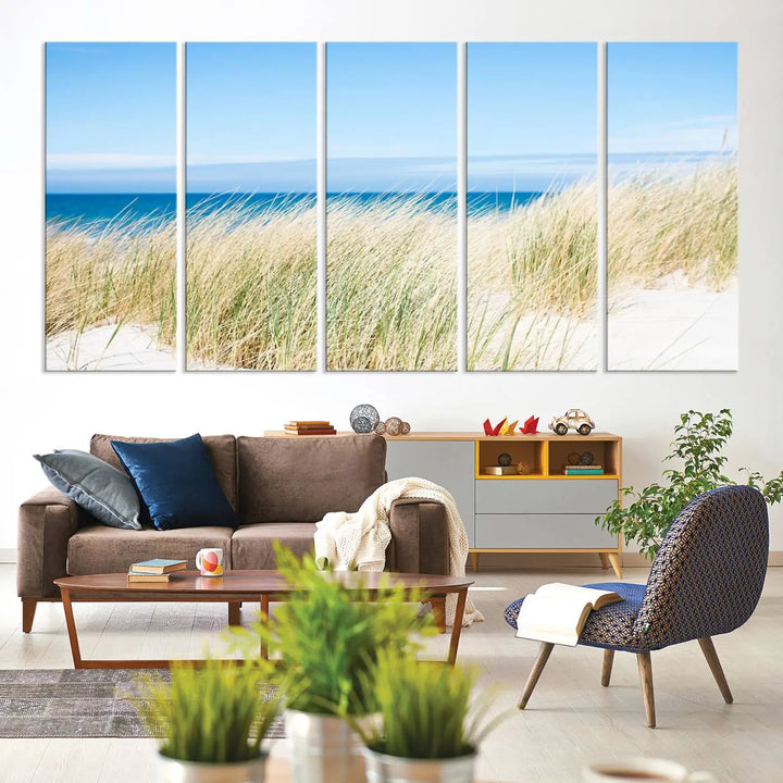 The Coastal Ocean Beach Wall Art Canvas Print, featuring a three-panel design with beach grass and an ocean view on museum-quality canvas, enhances the space in a modern living room. The artwork is ready to hang and comes with a UV-protective coating for enduring beauty.