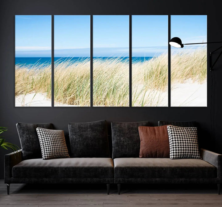 The Coastal Ocean Beach Wall Art Canvas Print, featuring a three-panel design with beach grass and an ocean view on museum-quality canvas, enhances the space in a modern living room. The artwork is ready to hang and comes with a UV-protective coating for enduring beauty.