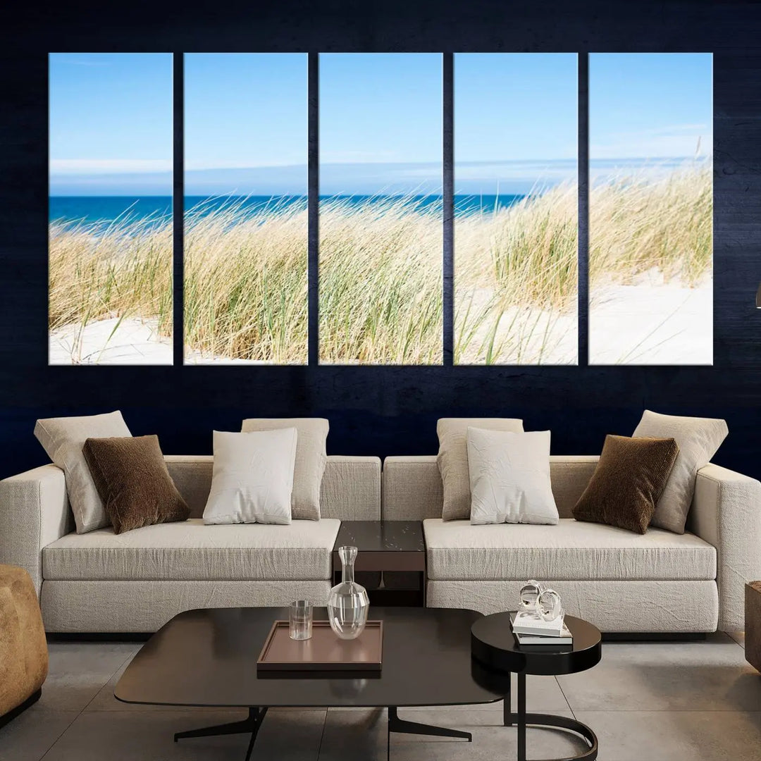 The Coastal Ocean Beach Wall Art Canvas Print, featuring a three-panel design with beach grass and an ocean view on museum-quality canvas, enhances the space in a modern living room. The artwork is ready to hang and comes with a UV-protective coating for enduring beauty.