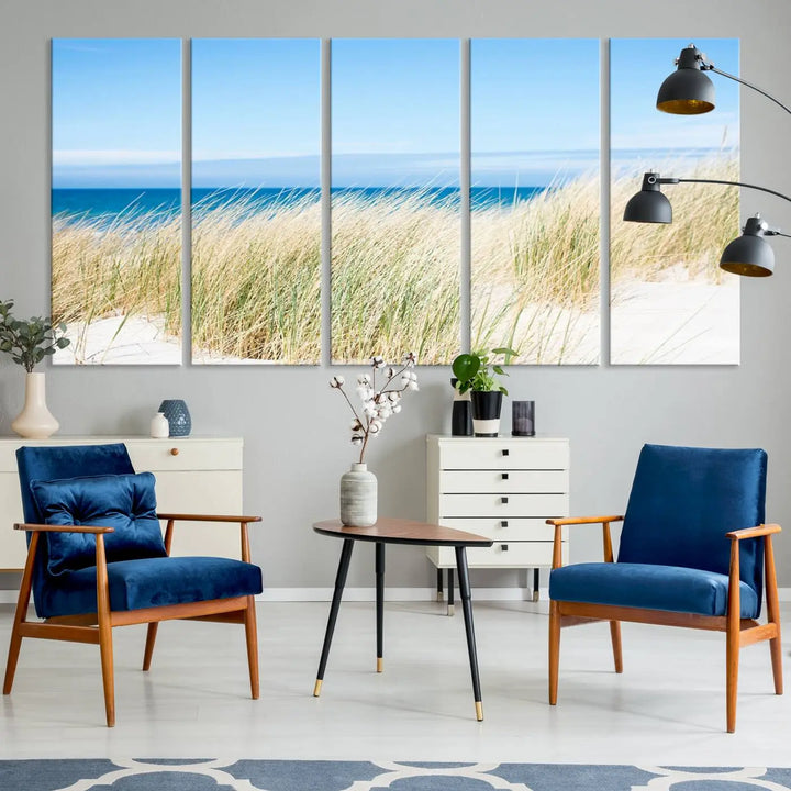 The Coastal Ocean Beach Wall Art Canvas Print, featuring a three-panel design with beach grass and an ocean view on museum-quality canvas, enhances the space in a modern living room. The artwork is ready to hang and comes with a UV-protective coating for enduring beauty.