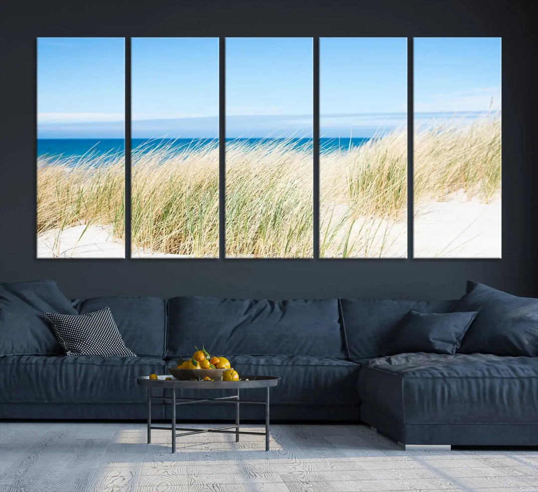 The Coastal Ocean Beach Wall Art Canvas Print, featuring a three-panel design with beach grass and an ocean view on museum-quality canvas, enhances the space in a modern living room. The artwork is ready to hang and comes with a UV-protective coating for enduring beauty.