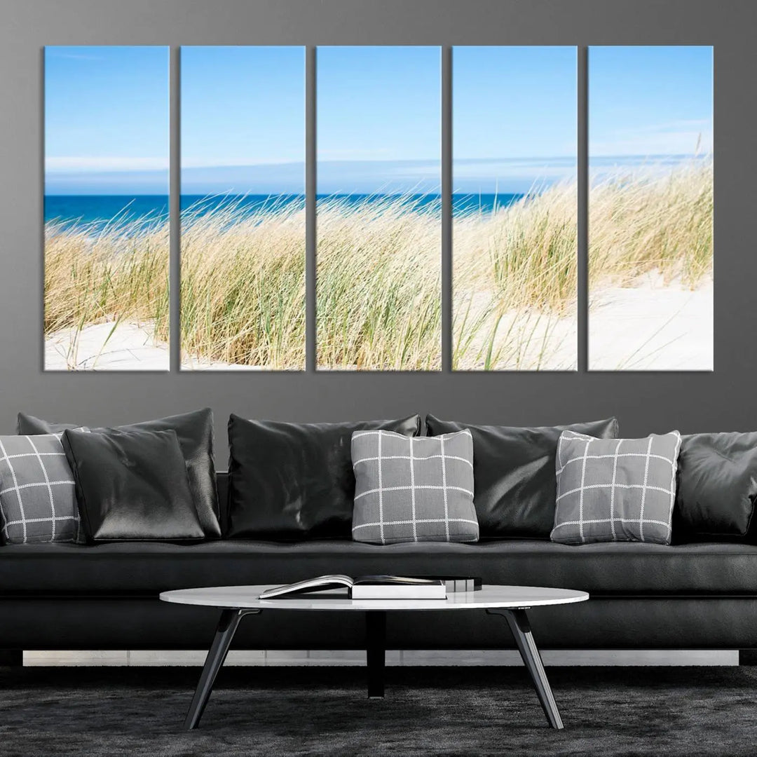 The Coastal Ocean Beach Wall Art Canvas Print, featuring a three-panel design with beach grass and an ocean view on museum-quality canvas, enhances the space in a modern living room. The artwork is ready to hang and comes with a UV-protective coating for enduring beauty.