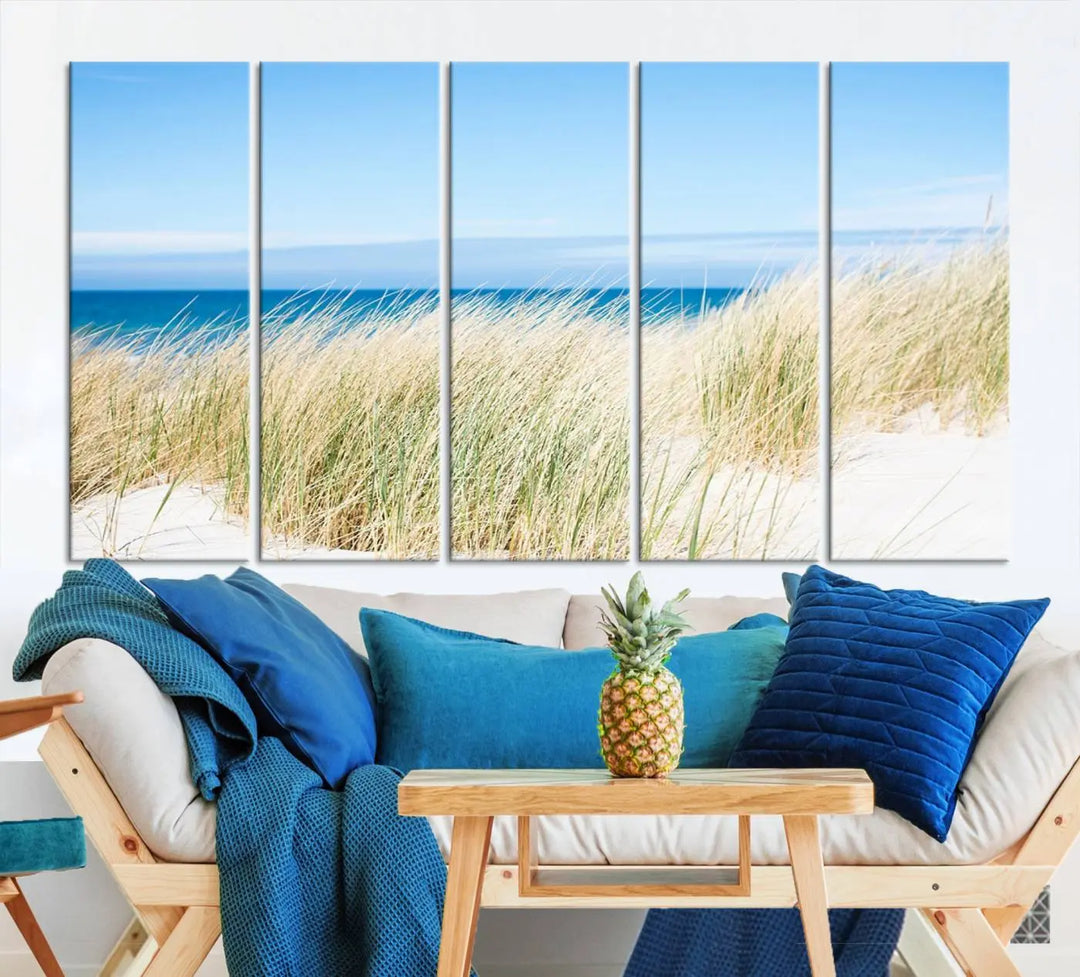 The Coastal Ocean Beach Wall Art Canvas Print, featuring a three-panel design with beach grass and an ocean view on museum-quality canvas, enhances the space in a modern living room. The artwork is ready to hang and comes with a UV-protective coating for enduring beauty.