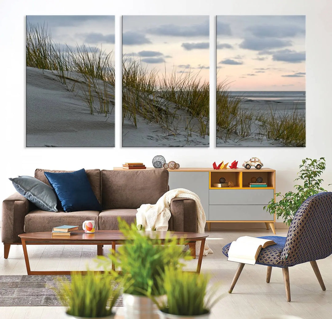 The Coastal Ocean Landscape Beach Wall Art Canvas Print is a triptych depicting sandy dunes and grass at sunset. It arrives ready to hang and is equipped with a UV-protective coating for lasting vibrancy and protection against fading sunlight.