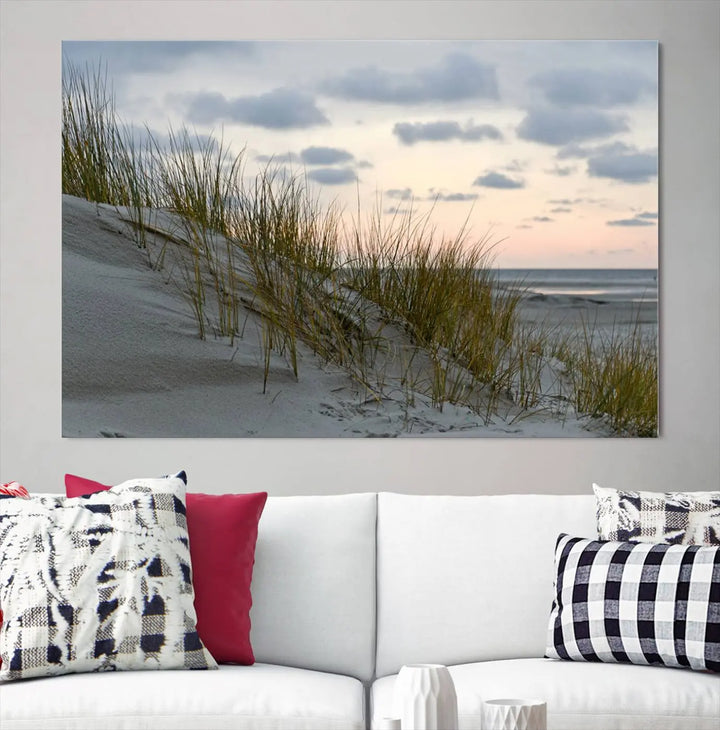 The Coastal Ocean Landscape Beach Wall Art Canvas Print is a triptych depicting sandy dunes and grass at sunset. It arrives ready to hang and is equipped with a UV-protective coating for lasting vibrancy and protection against fading sunlight.