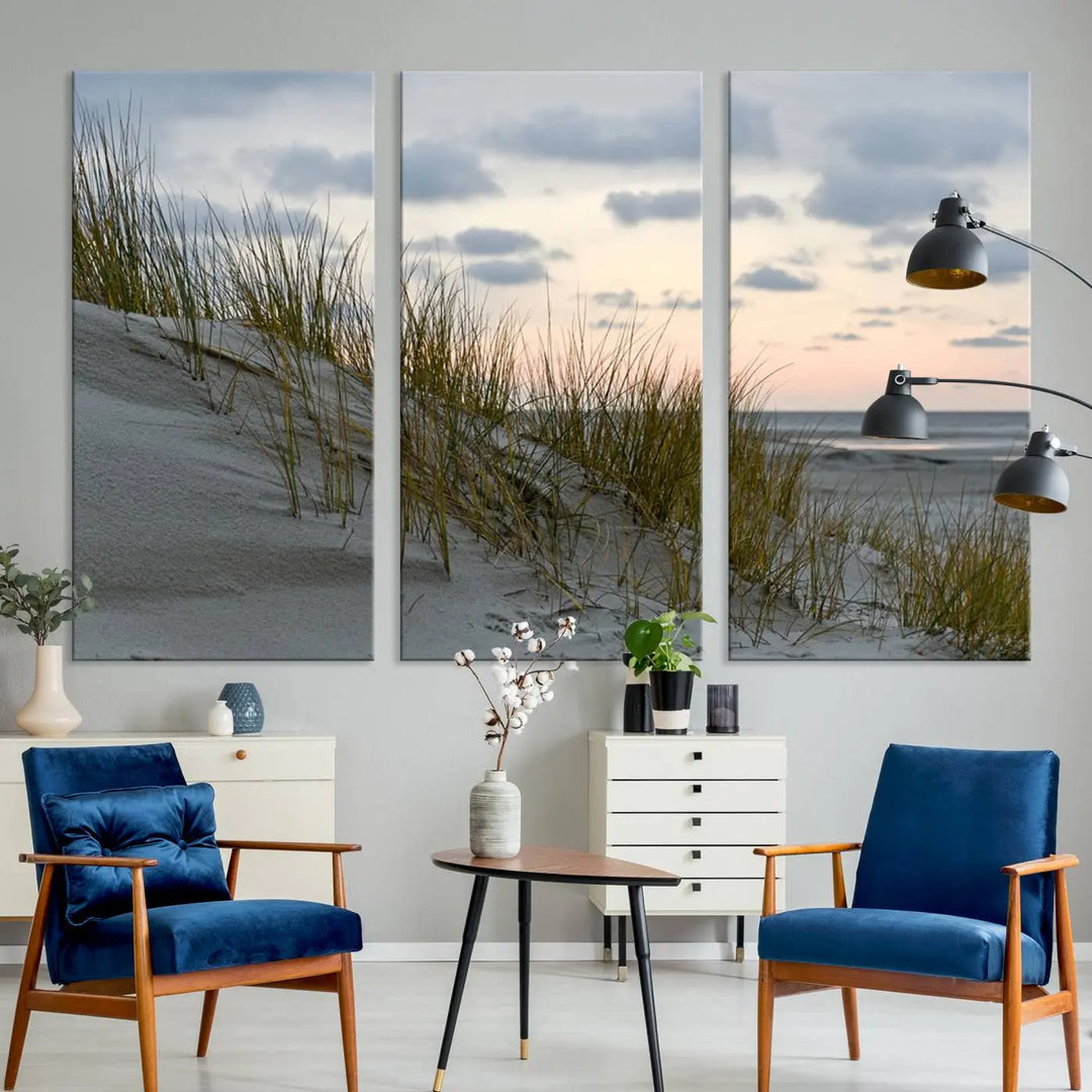 The Coastal Ocean Landscape Beach Wall Art Canvas Print is a triptych depicting sandy dunes and grass at sunset. It arrives ready to hang and is equipped with a UV-protective coating for lasting vibrancy and protection against fading sunlight.