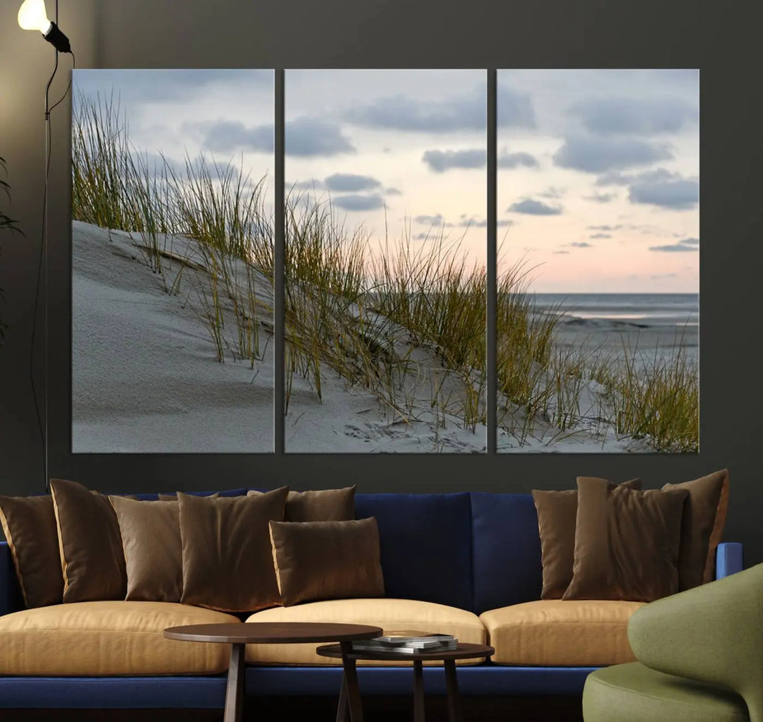 The Coastal Ocean Landscape Beach Wall Art Canvas Print is a triptych depicting sandy dunes and grass at sunset. It arrives ready to hang and is equipped with a UV-protective coating for lasting vibrancy and protection against fading sunlight.