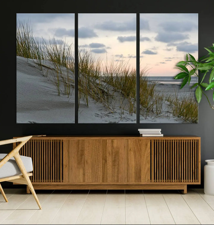 The Coastal Ocean Landscape Beach Wall Art Canvas Print is a triptych depicting sandy dunes and grass at sunset. It arrives ready to hang and is equipped with a UV-protective coating for lasting vibrancy and protection against fading sunlight.