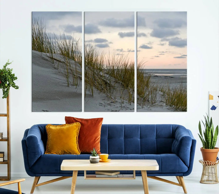 The Coastal Ocean Landscape Beach Wall Art Canvas Print is a triptych depicting sandy dunes and grass at sunset. It arrives ready to hang and is equipped with a UV-protective coating for lasting vibrancy and protection against fading sunlight.