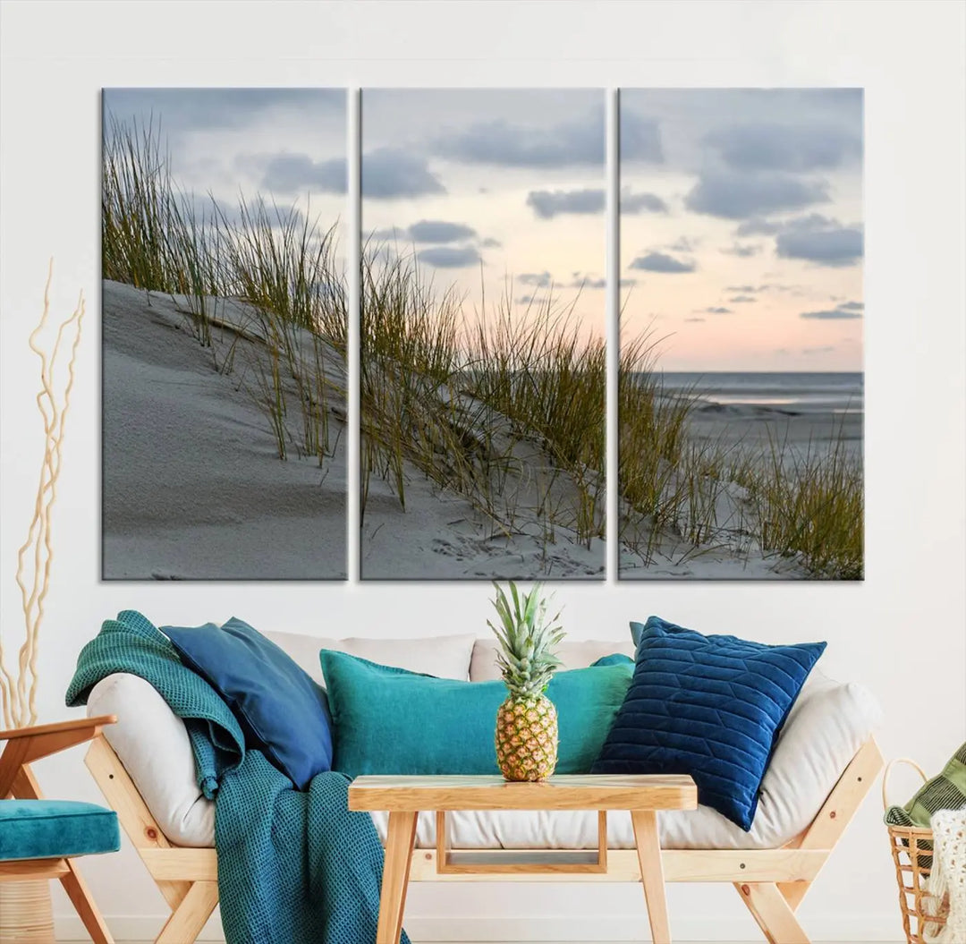 The Coastal Ocean Landscape Beach Wall Art Canvas Print is a triptych depicting sandy dunes and grass at sunset. It arrives ready to hang and is equipped with a UV-protective coating for lasting vibrancy and protection against fading sunlight.