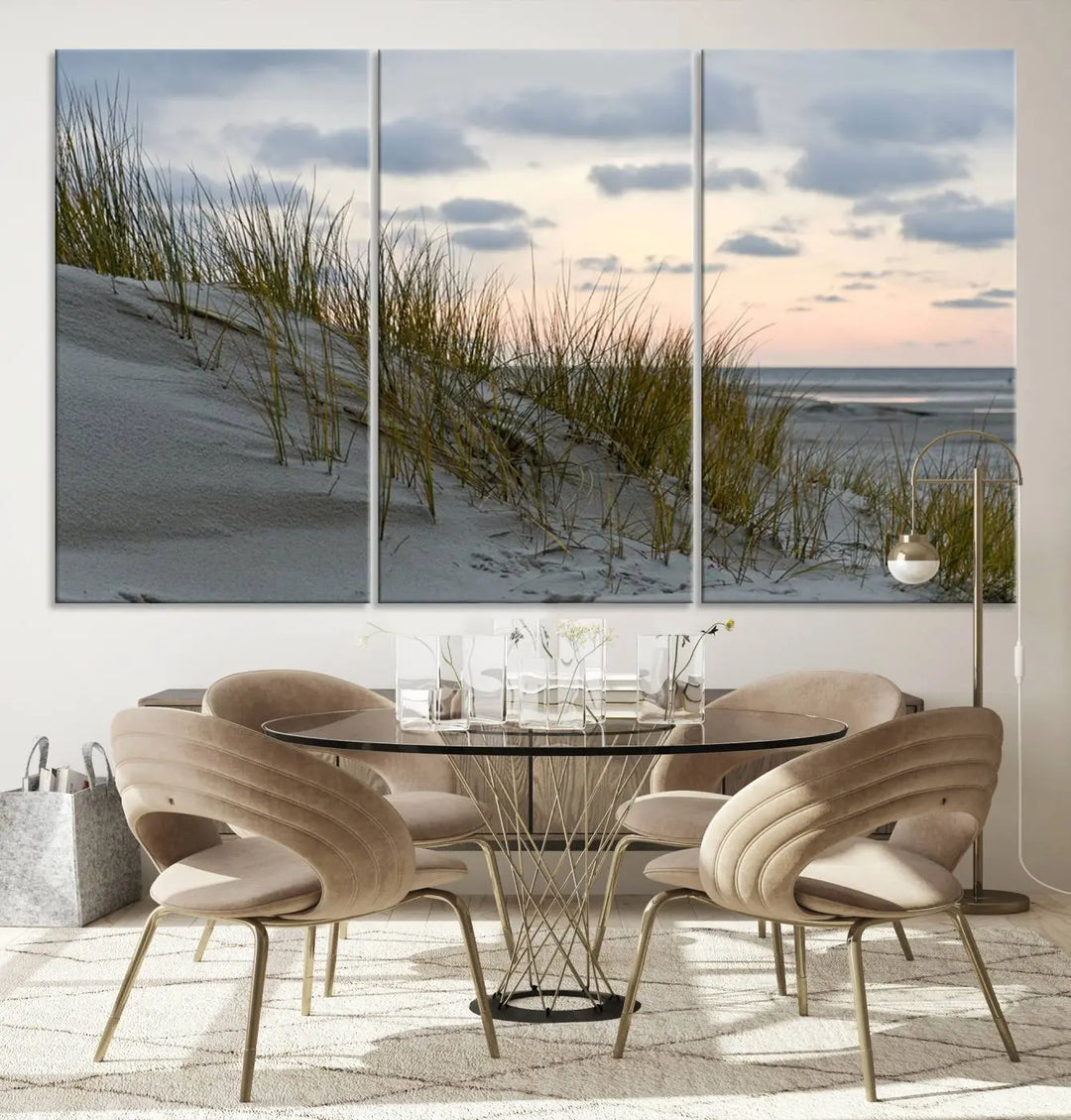 The Coastal Ocean Landscape Beach Wall Art Canvas Print is a triptych depicting sandy dunes and grass at sunset. It arrives ready to hang and is equipped with a UV-protective coating for lasting vibrancy and protection against fading sunlight.