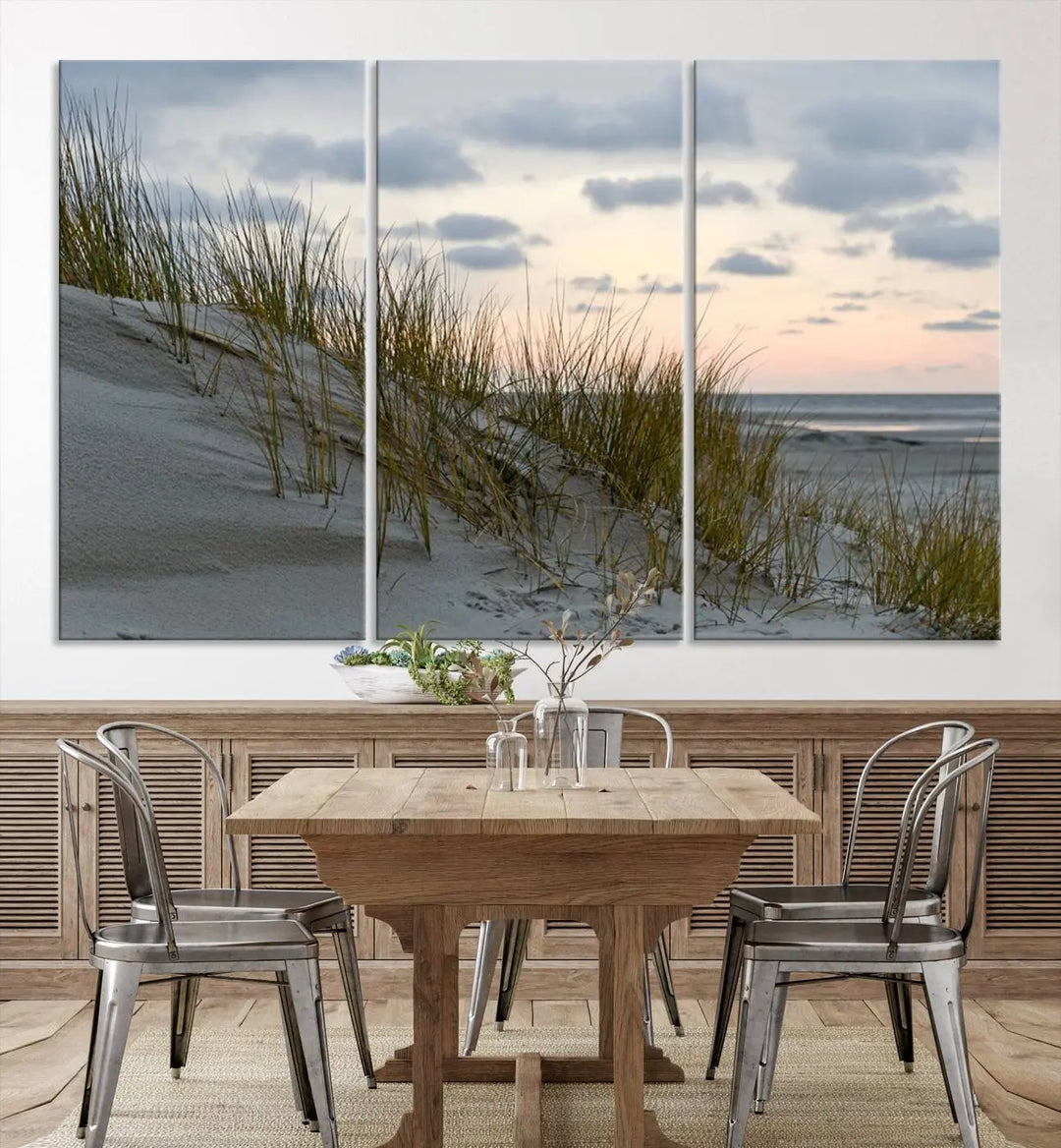 The Coastal Ocean Landscape Beach Wall Art Canvas Print is a triptych depicting sandy dunes and grass at sunset. It arrives ready to hang and is equipped with a UV-protective coating for lasting vibrancy and protection against fading sunlight.