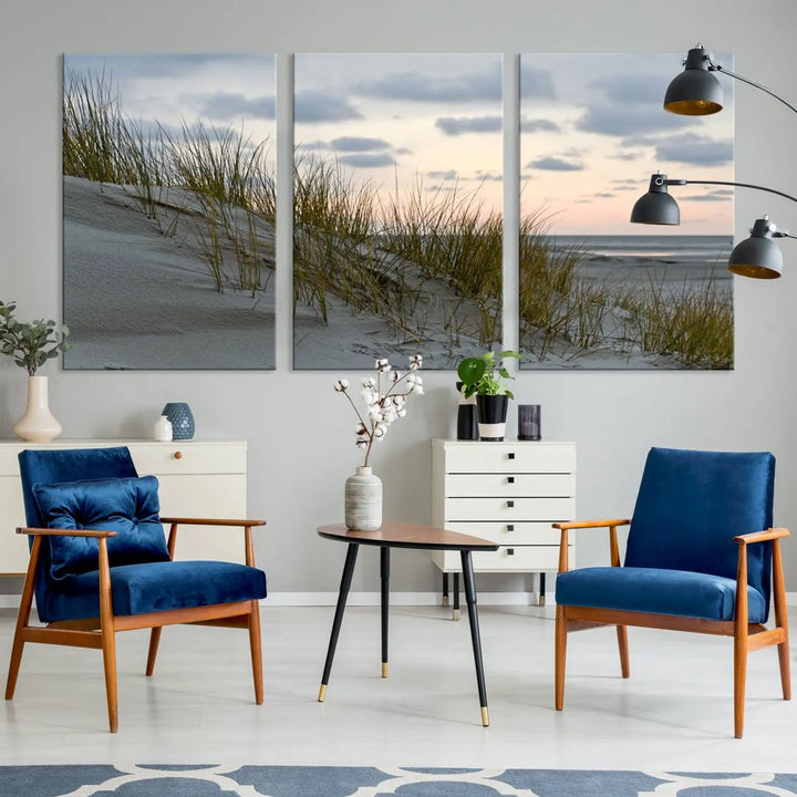 The Coastal Ocean Landscape Beach Wall Art Canvas Print is a triptych depicting sandy dunes and grass at sunset. It arrives ready to hang and is equipped with a UV-protective coating for lasting vibrancy and protection against fading sunlight.