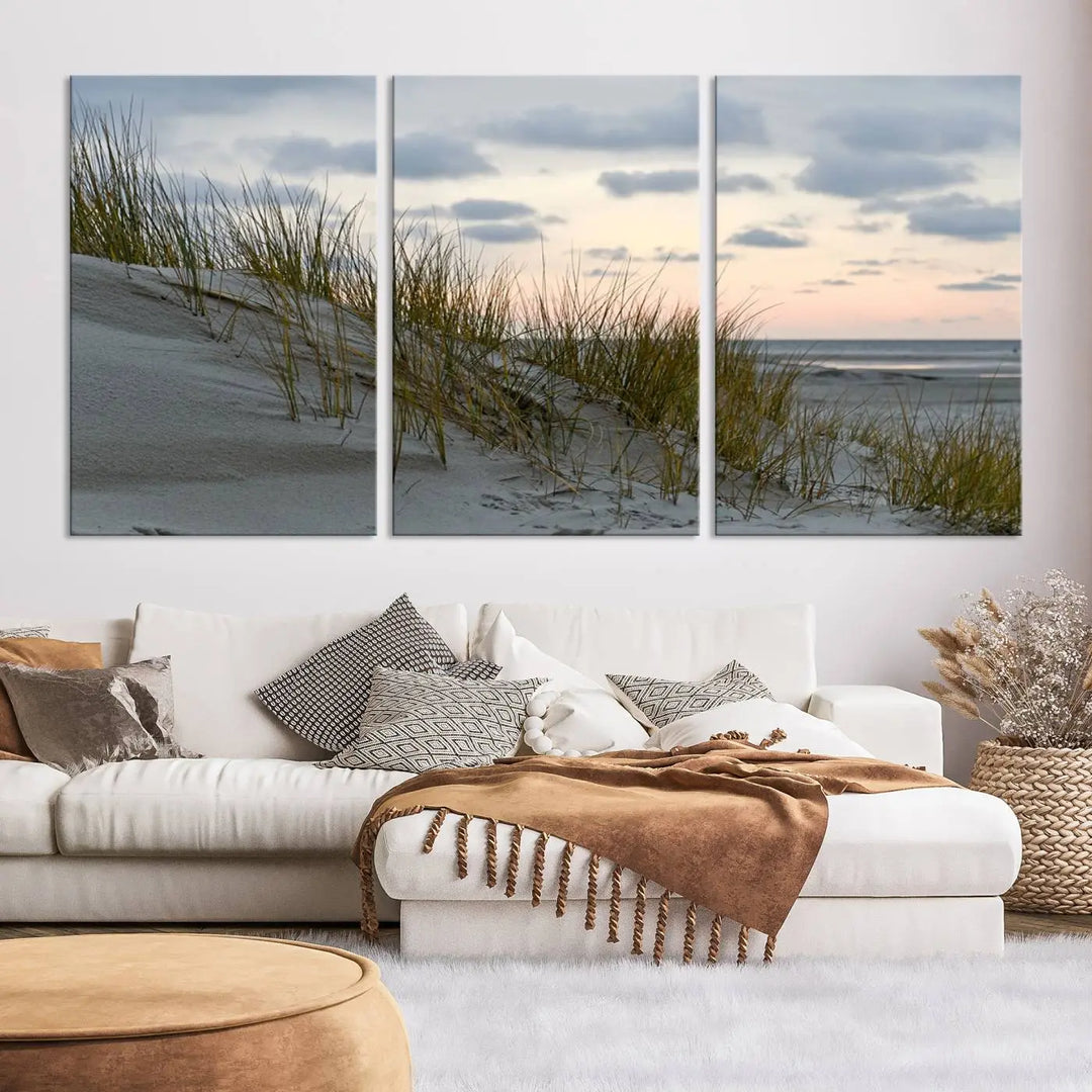 The Coastal Ocean Landscape Beach Wall Art Canvas Print is a triptych depicting sandy dunes and grass at sunset. It arrives ready to hang and is equipped with a UV-protective coating for lasting vibrancy and protection against fading sunlight.