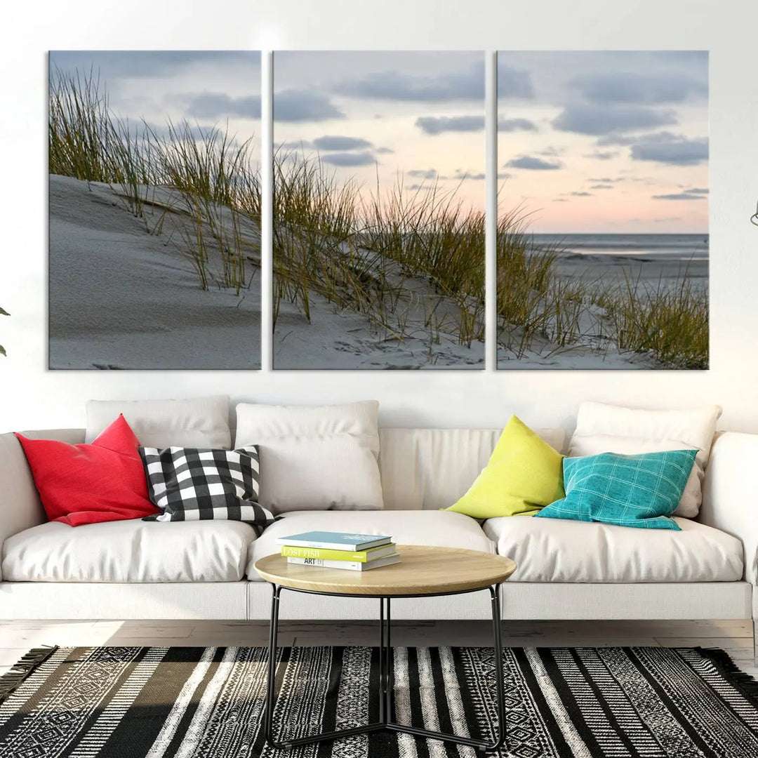 The Coastal Ocean Landscape Beach Wall Art Canvas Print is a triptych depicting sandy dunes and grass at sunset. It arrives ready to hang and is equipped with a UV-protective coating for lasting vibrancy and protection against fading sunlight.