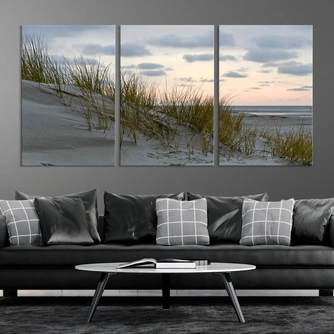 The Coastal Ocean Landscape Beach Wall Art Canvas Print is a triptych depicting sandy dunes and grass at sunset. It arrives ready to hang and is equipped with a UV-protective coating for lasting vibrancy and protection against fading sunlight.