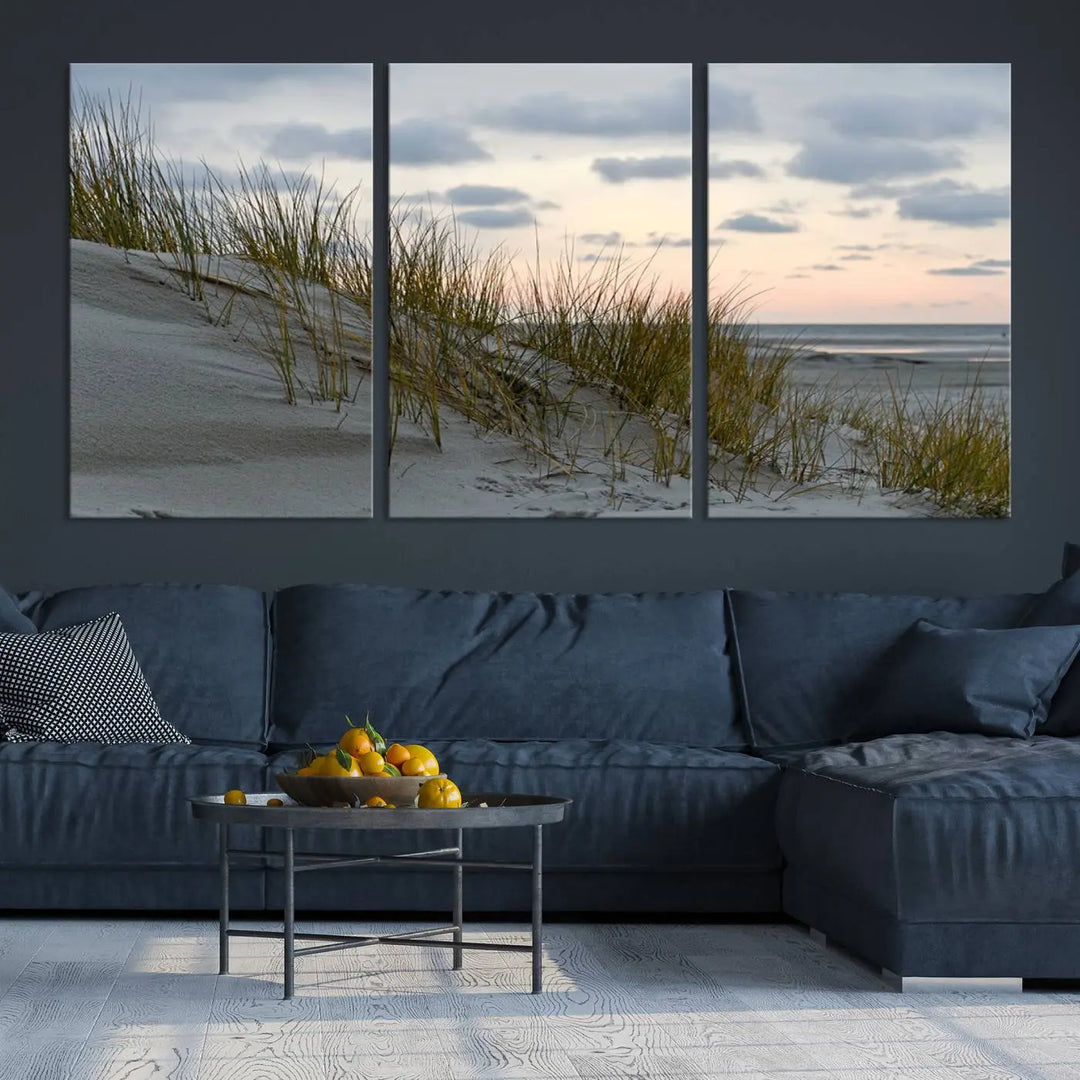 The Coastal Ocean Landscape Beach Wall Art Canvas Print is a triptych depicting sandy dunes and grass at sunset. It arrives ready to hang and is equipped with a UV-protective coating for lasting vibrancy and protection against fading sunlight.