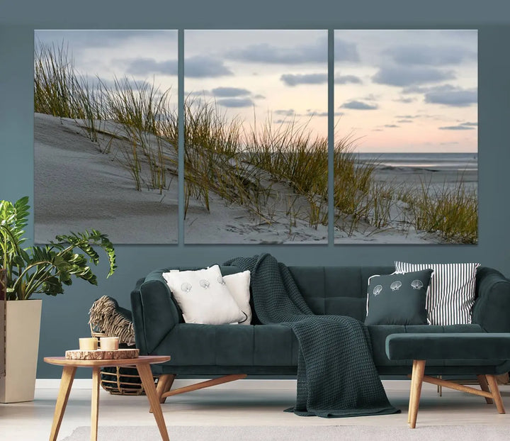 The Coastal Ocean Landscape Beach Wall Art Canvas Print is a triptych depicting sandy dunes and grass at sunset. It arrives ready to hang and is equipped with a UV-protective coating for lasting vibrancy and protection against fading sunlight.