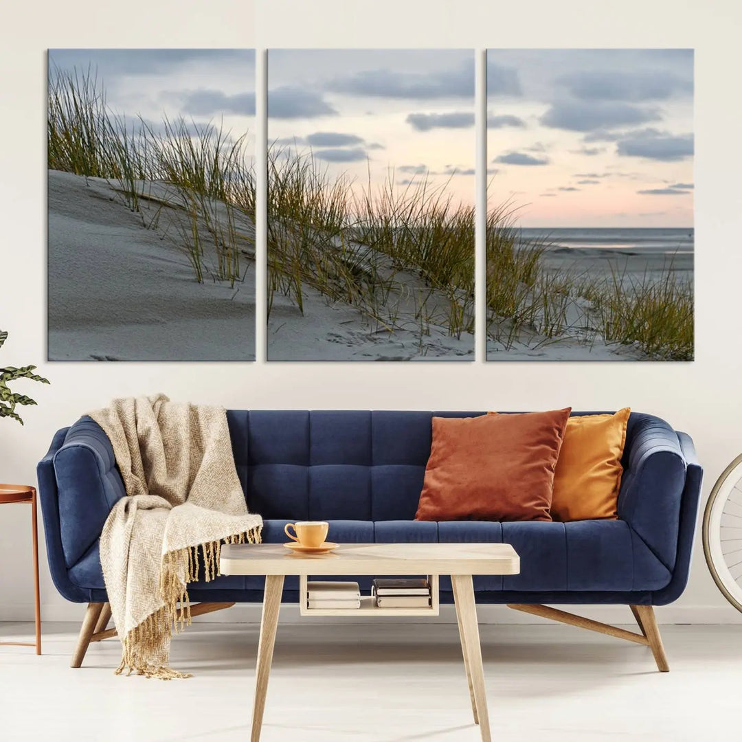 The Coastal Ocean Landscape Beach Wall Art Canvas Print is a triptych depicting sandy dunes and grass at sunset. It arrives ready to hang and is equipped with a UV-protective coating for lasting vibrancy and protection against fading sunlight.