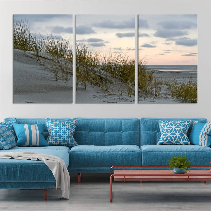 The Coastal Ocean Landscape Beach Wall Art Canvas Print is a triptych depicting sandy dunes and grass at sunset. It arrives ready to hang and is equipped with a UV-protective coating for lasting vibrancy and protection against fading sunlight.