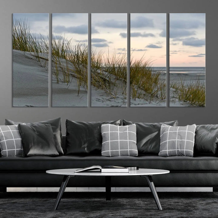 The Coastal Ocean Landscape Beach Wall Art Canvas Print is a triptych depicting sandy dunes and grass at sunset. It arrives ready to hang and is equipped with a UV-protective coating for lasting vibrancy and protection against fading sunlight.