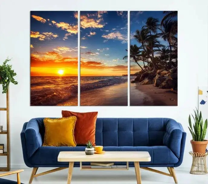 A Coastal Wall Art Beach at Sunset Canvas Print, featuring a triptych of a tropical sunset over the ocean with palm trees, graces the room.