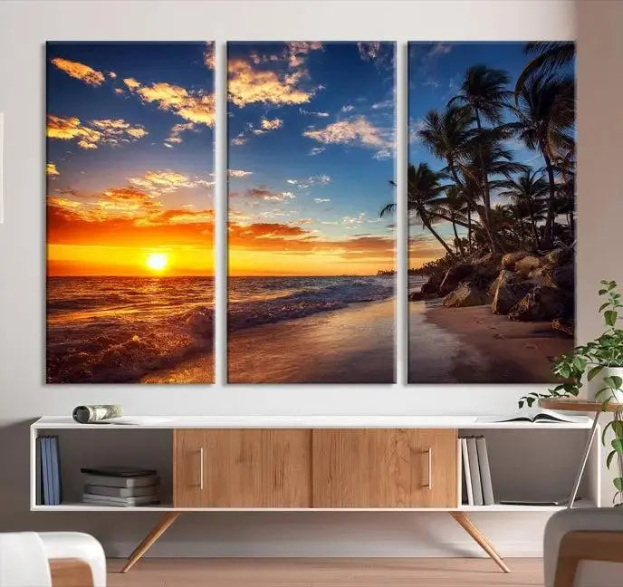 A Coastal Wall Art Beach at Sunset Canvas Print, featuring a triptych of a tropical sunset over the ocean with palm trees, graces the room.