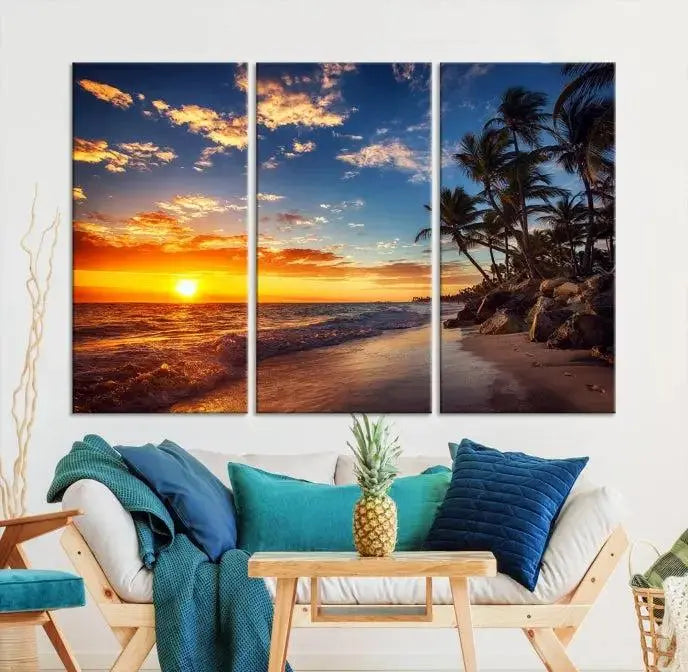 A Coastal Wall Art Beach at Sunset Canvas Print, featuring a triptych of a tropical sunset over the ocean with palm trees, graces the room.