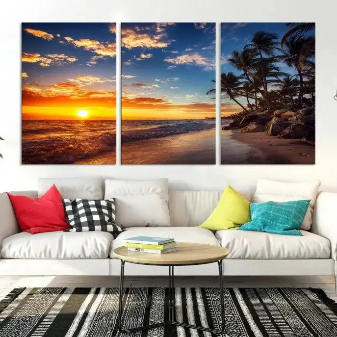 A Coastal Wall Art Beach at Sunset Canvas Print, featuring a triptych of a tropical sunset over the ocean with palm trees, graces the room.