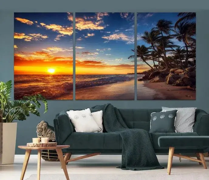 A Coastal Wall Art Beach at Sunset Canvas Print, featuring a triptych of a tropical sunset over the ocean with palm trees, graces the room.