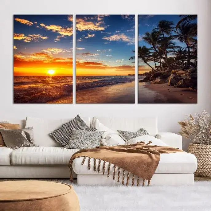 A Coastal Wall Art Beach at Sunset Canvas Print, featuring a triptych of a tropical sunset over the ocean with palm trees, graces the room.