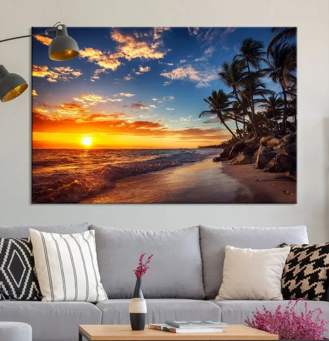 A Coastal Wall Art Beach at Sunset Canvas Print, featuring a triptych of a tropical sunset over the ocean with palm trees, graces the room.