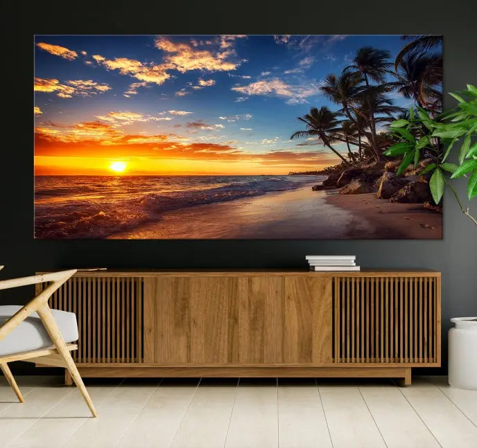 A Coastal Wall Art Beach at Sunset Canvas Print, featuring a triptych of a tropical sunset over the ocean with palm trees, graces the room.