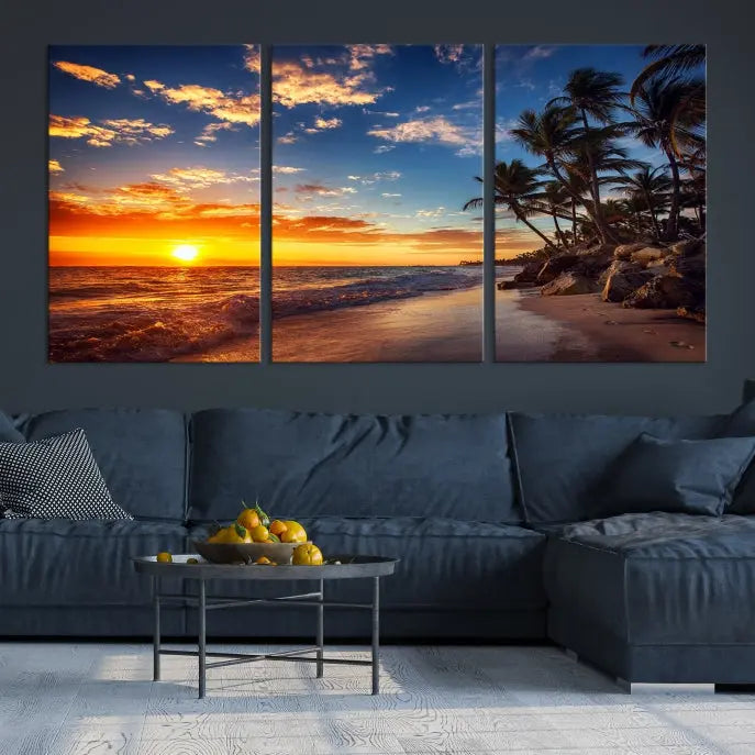 A Coastal Wall Art Beach at Sunset Canvas Print, featuring a triptych of a tropical sunset over the ocean with palm trees, graces the room.