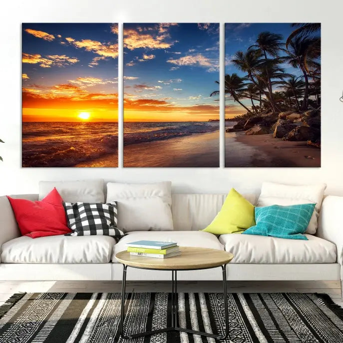 A Coastal Wall Art Beach at Sunset Canvas Print, featuring a triptych of a tropical sunset over the ocean with palm trees, graces the room.