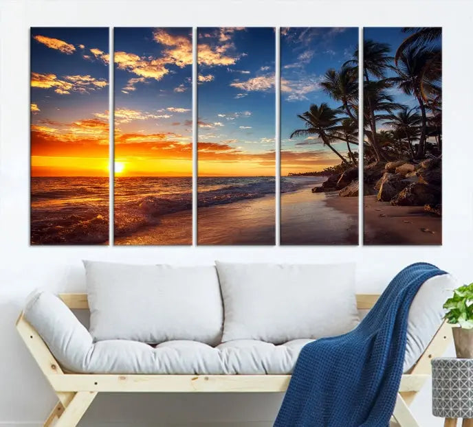 A Coastal Wall Art Beach at Sunset Canvas Print, featuring a triptych of a tropical sunset over the ocean with palm trees, graces the room.